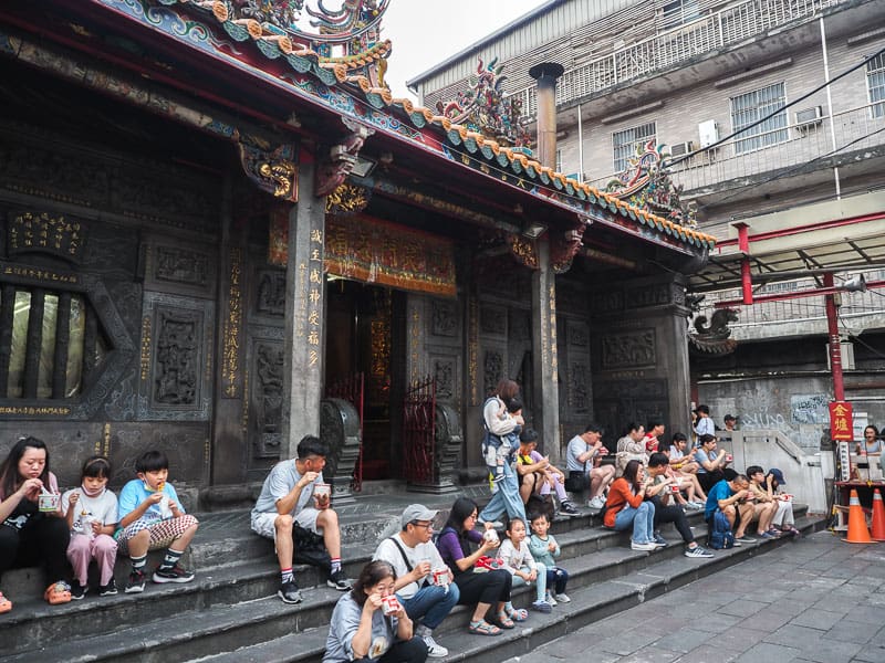 Several people sitting on the stairs of a temple eating food
