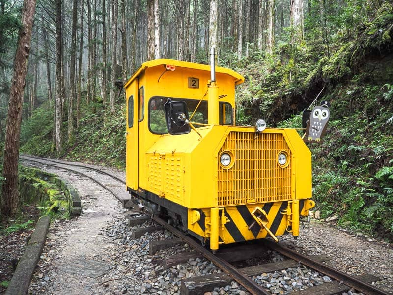 A single bright yellow train engine car on a track in the forest