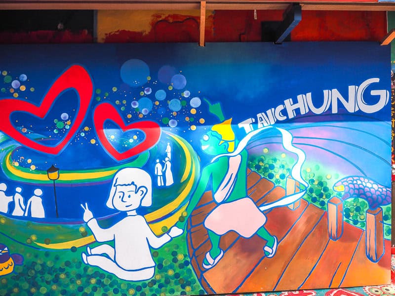 A painted mural that says Taichung, has a girl on it, some red hearts, and other local scenes