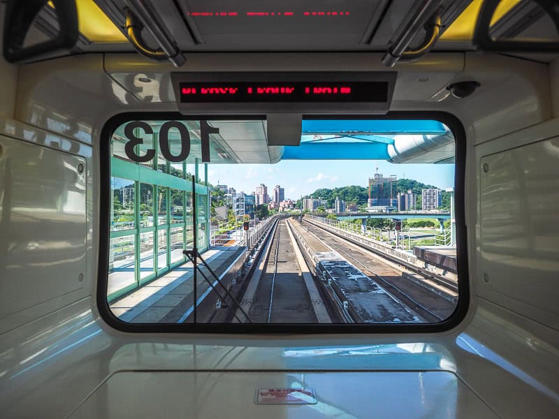 Looking out the rectangular front window of an MRT line, with the tracks going forward then curving at the end, and station platform visible on left side