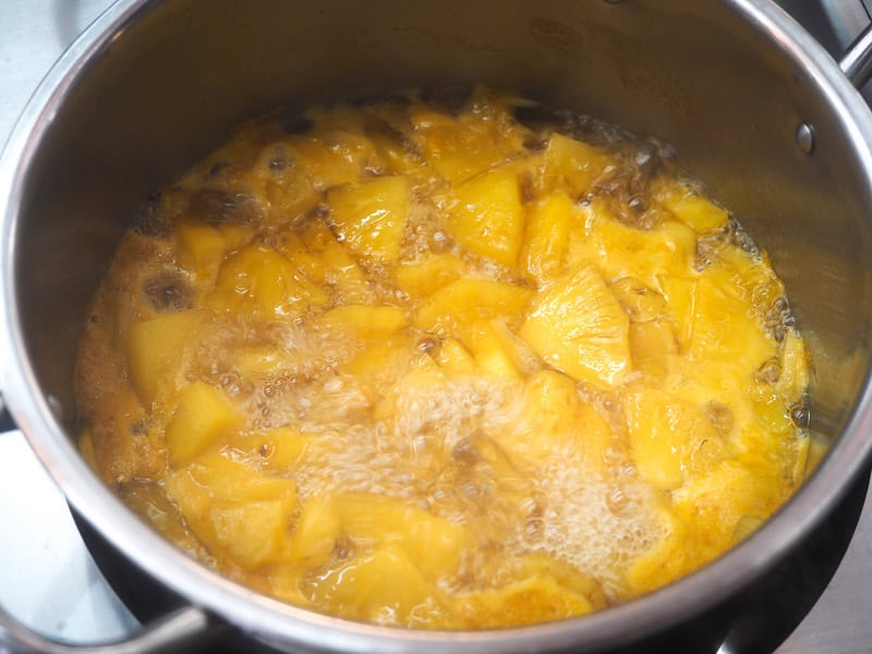 Looking into to a large metal pot full of chunks of pineapple in boiling water