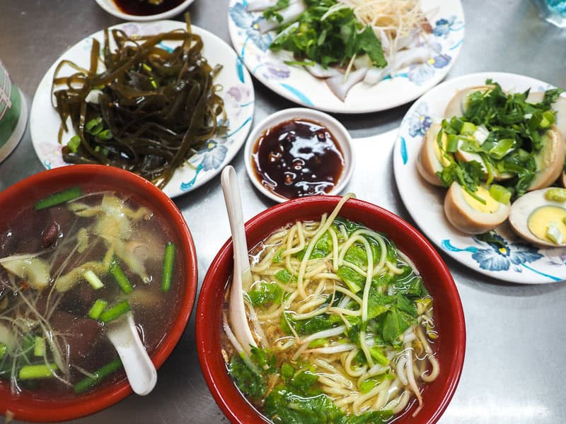 A metal table with half a dozen noodle, seaweed, and egg dishes on it