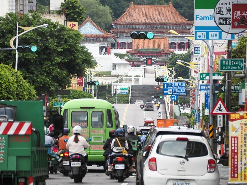 Looking up a busy road with lots of motorcycles and vehicles, with a temple on a hill at the end of the road