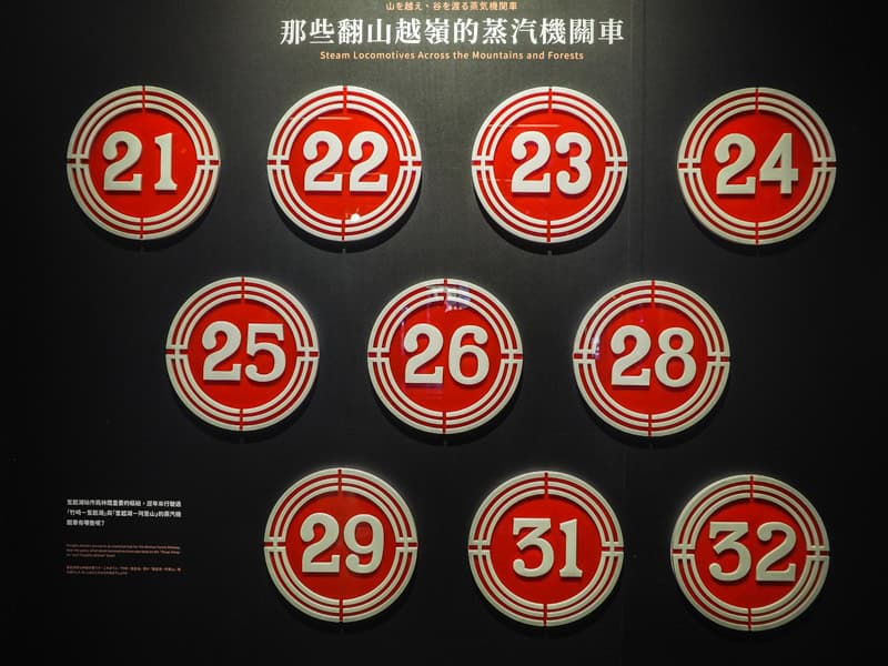 A black wall with several round train numbers in red