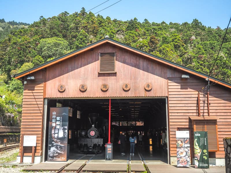 A large train shed turned museum for the Alishan Forest Railway, with its door open and some trains and tourists visible inside