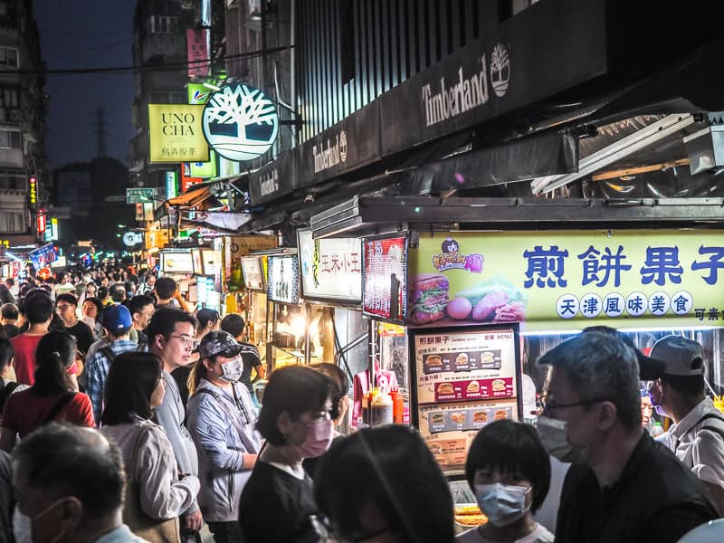 Looking up one side of a night market street, with lots of food stalls and people in front of them