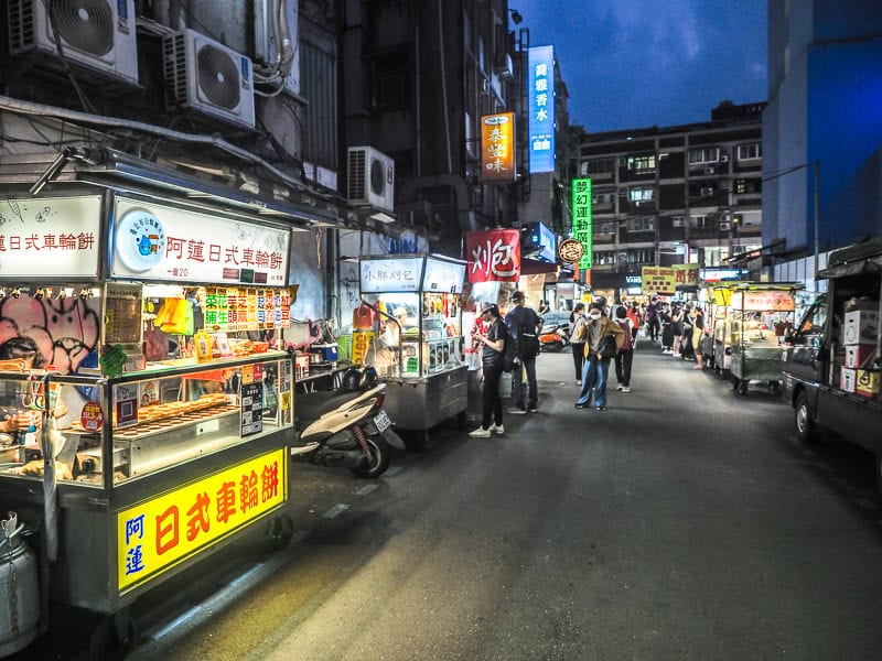 Looking down a night market street at night, with only a sprinkling of people visible down the road