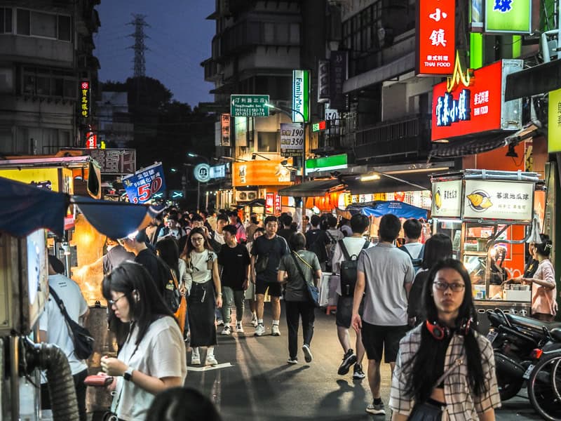 Gong Guan Night Market at night with many people walking down the street and vendors on either side