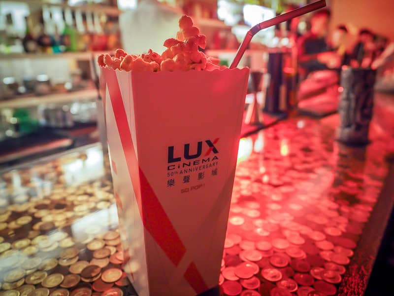 A box of movie theater popcorn on a bar, with a straw coming out of it