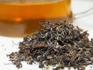 Close up of a pile of loose tea and clear bug of tea behind