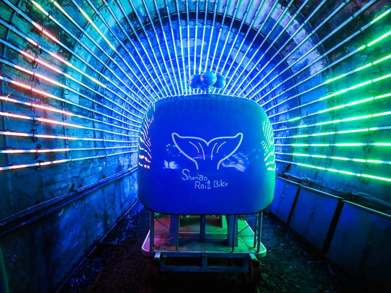 A blue rail bike going through a tunnel, with lines of colorful blue and pink lights lining the tunnel