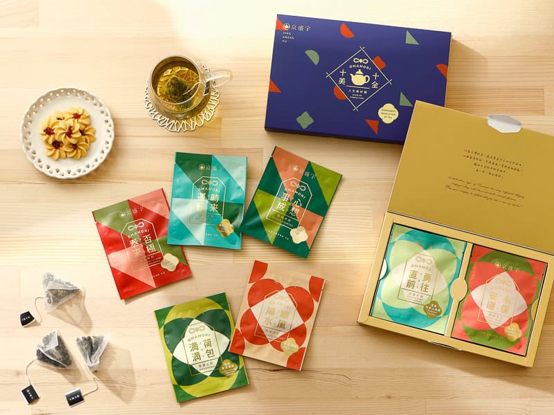 A variety of tea products on display on a wooden table, shot from above, include boxes of tea, tea bags, tea cup, and cookie