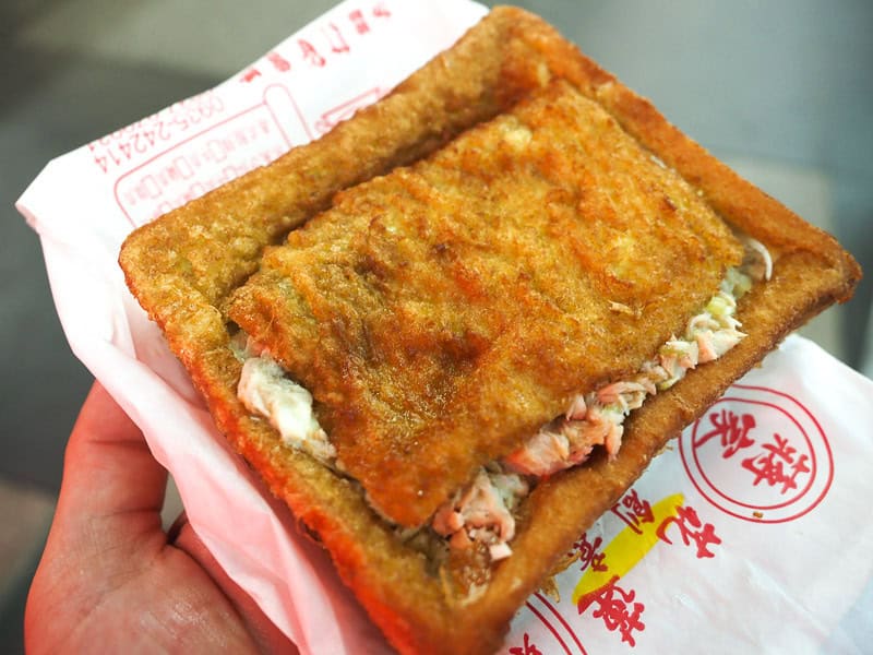 A hand holding up a large deep fried chunk of bread which has been cut open and stuffed with tuna