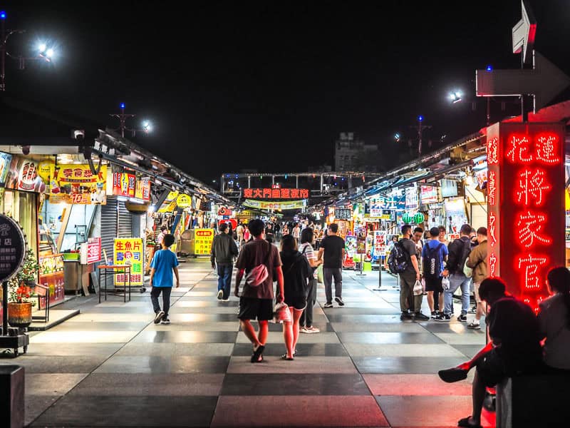 A night market scene in Dongdamen Night Market Hualien with some people walking along a checker patterned floor and food stalls on either side