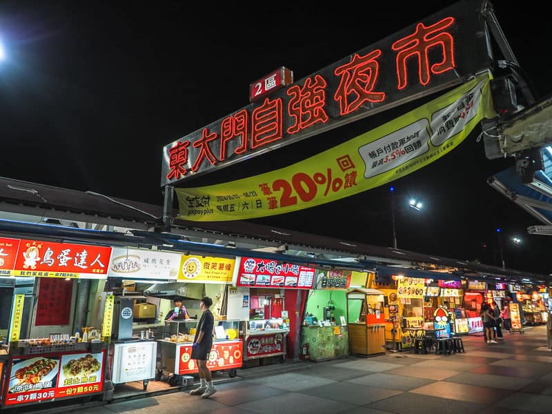 A row of night market vendors with neon red Chinese characters above