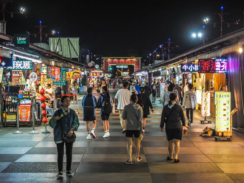 Looking up a pedestrian street in Dongdamen Night Market with some people walking down it and food stalls on either side.