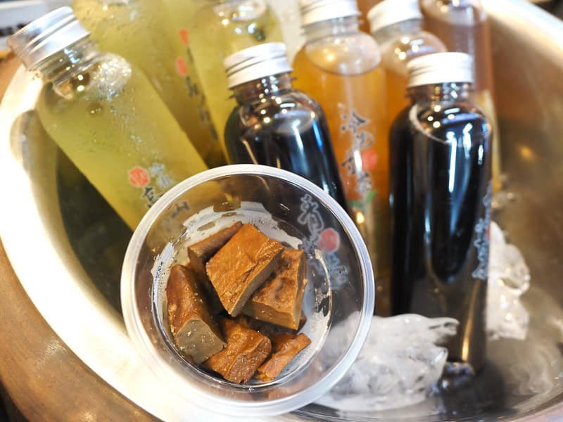 Looking down at a plastic cup of tofu chunks and some bottles of herbal drinks at a night market food stall