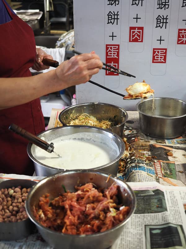 Close up of a vendor's mid-section and hands as they prepare an oyster cake, with various bowls of ingredients in front of them
