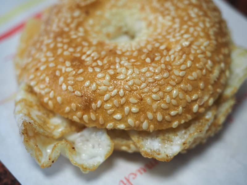Close up of bagel-like bun topped with sesame seeds and filled with egg