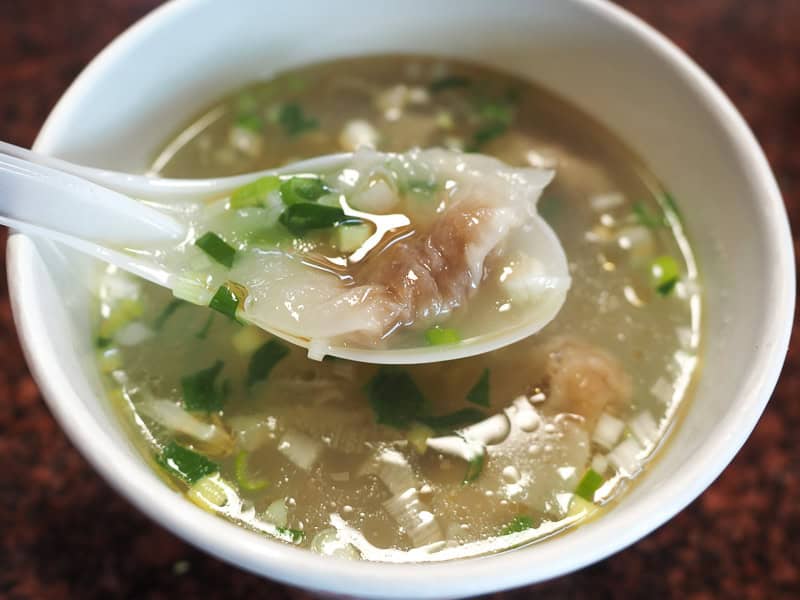 Close up of a bowl of pork dumpling soup with a white spoon holding up one of the dumplings