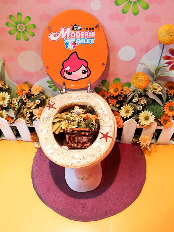 A toilet decorated to contain flowers, stickers, and the words "Modern Toilet" in the entrance to the restaurant