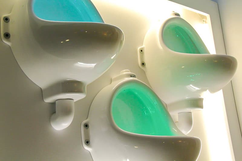 Three porcelain toilets hung on a bathroom wall as decorations, with green and blue lights coming from inside them