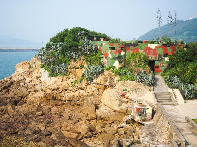 A small fort painted in green and red camouflage built on a rocky point on the coast
