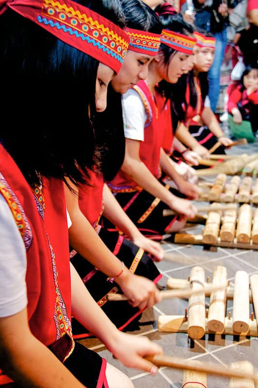 Vertical image of Taiwanese youths kneeling on the ground and playing wooden instruments