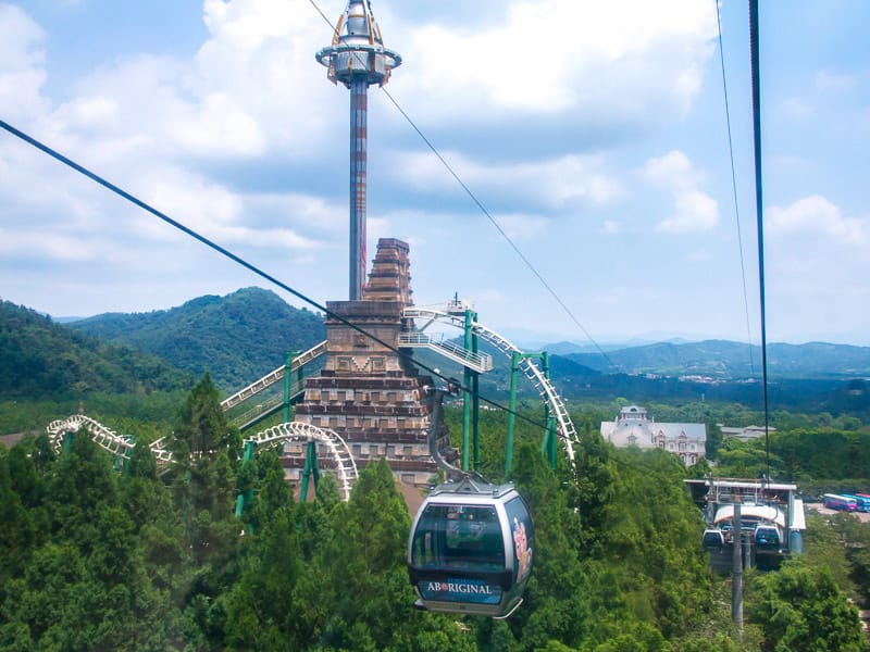 Some gondolas descending into a theme park, going past some huge rides and rollercoasters