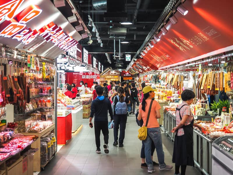 Some people shopping in an indoor traditional markets with shops selling dried goods on either side