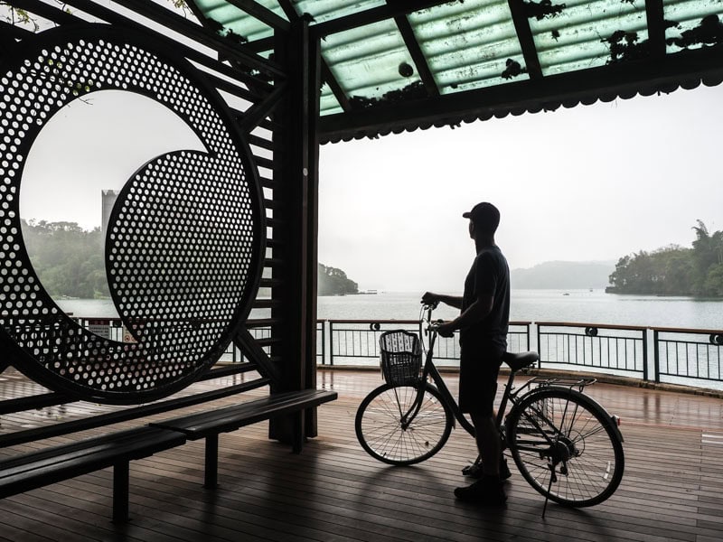 Nick Kembel in silhouette on a bicycle on a dock with moon design on it next to Sun Moon Lake