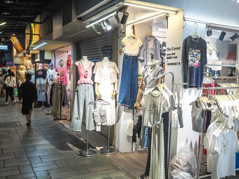 Looking down a street of cheap women's clothing stores at night, with some people walking by