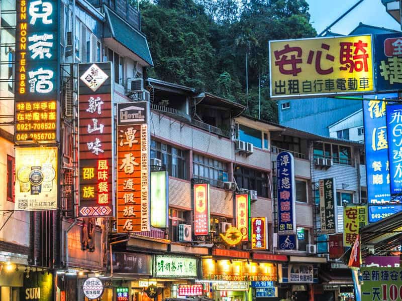 A row of shops and restaurants with lit up signs along the main road in Shuishe village