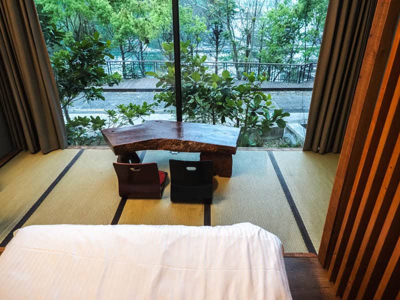 View of hotel room shot from the bed with low table on tatami floor and window looking out at trees and Sun Moon Lake