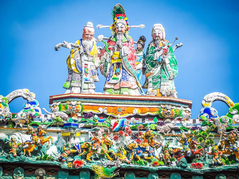 Zoomed in shot of three figures made out of colorful ceramic pieces on top of a temple