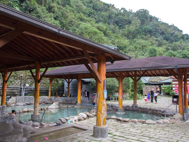 A small outdoor hot spring facility with wooden canopies over the tubs