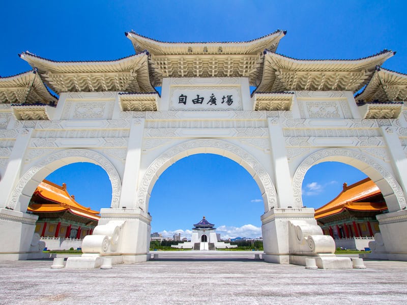 Looking through a large white arch at a square and Chiang Kai-Shek Memorial Hall