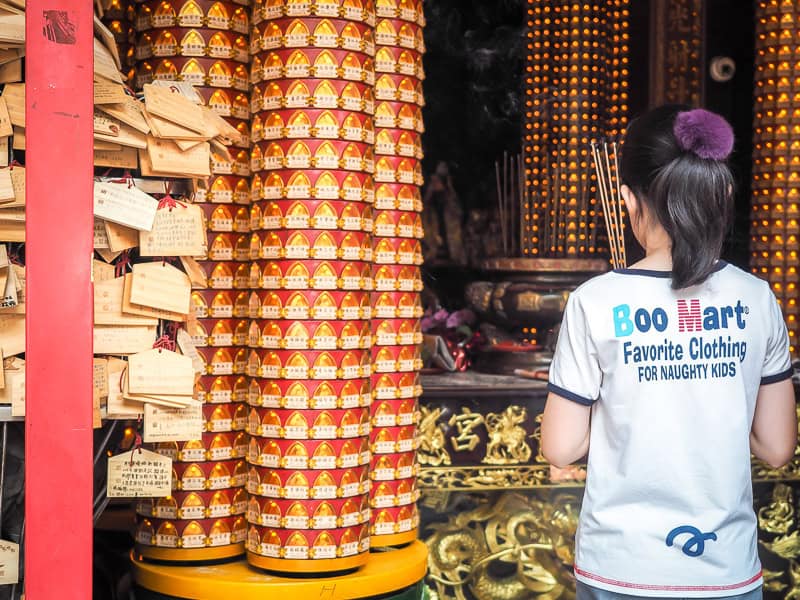 A child shot from behind as she holds incense and prays in front of a temple in Taipei