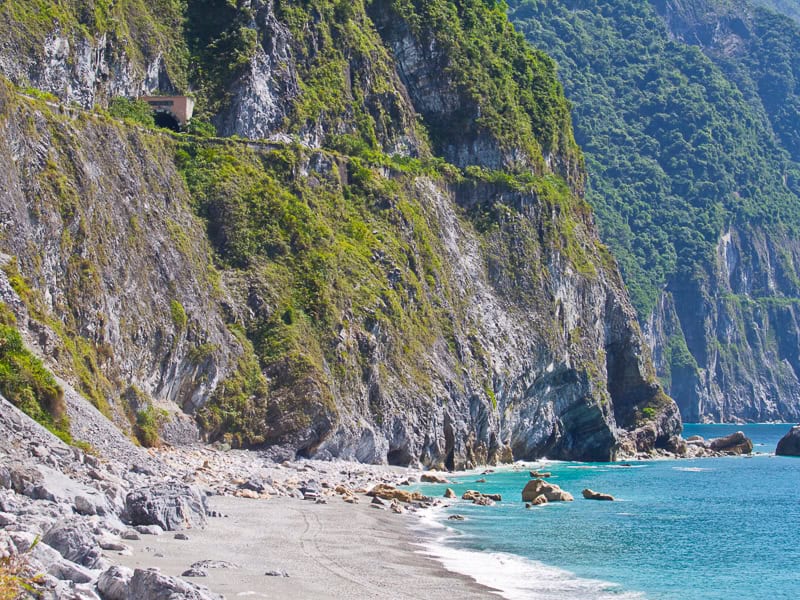 Looking from a beach to some coastal cliffs above the sea, with a road and tunnel visible