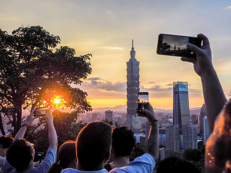 A group of tourists shot from behind as they take photos of the sunset over Taipei city and Taipei 101 from Elephant Mountain