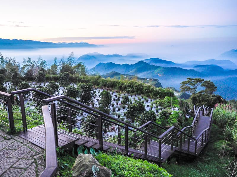 A viewpoint with a long wooden staircase going down and view of mountaintops in the valley below at sunrise
