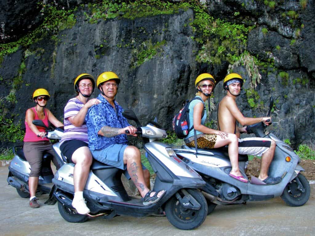 Nick Kembel and his family (two sisters and parents) sitting on three scooters next to a rocky cliff