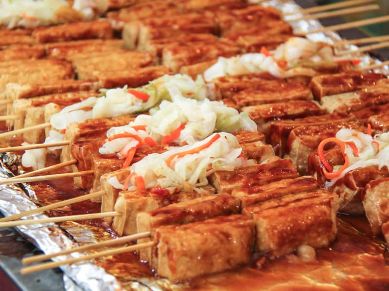 A tray covered in sticks of stinky tofu topped with pickled vegetables and sauce