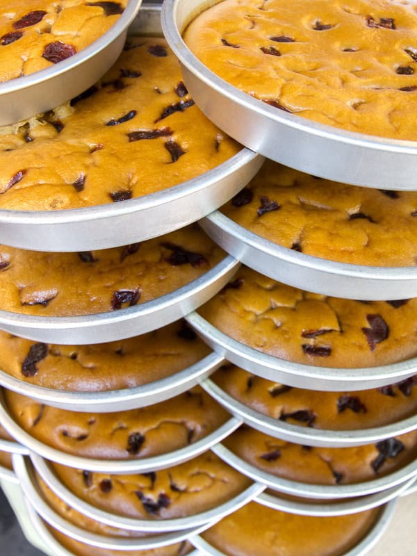 A tall stack of round metal tins of brown sugar cake with dried fruits baked into them