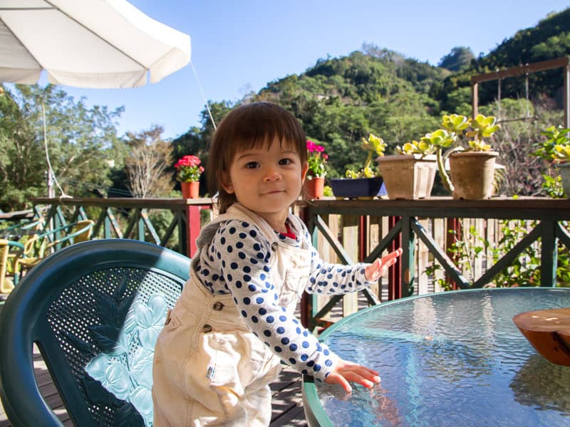 A young girl standing on her chair at a round glass table on a B&B patio