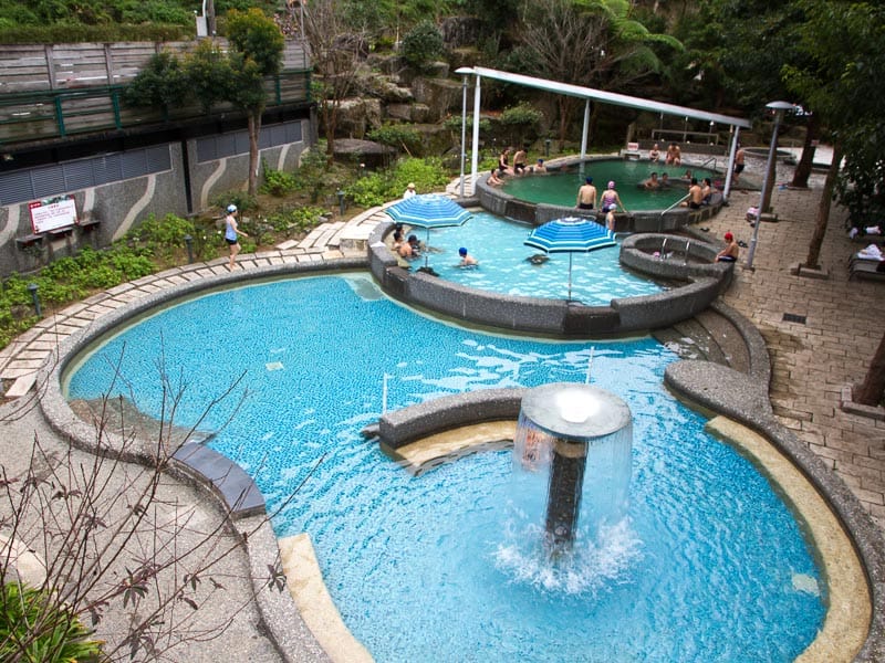 Looking down on a large blue outdoor hot spring pool with some people in a side pool