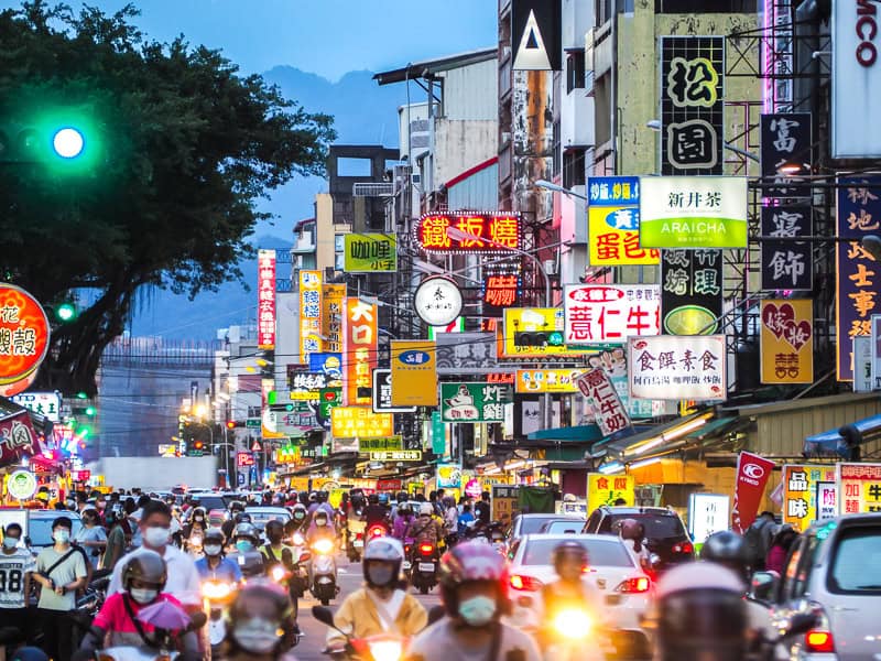 A very busy street in Kaohsiung, crowded with cars and scooters, with many shops signs on the side