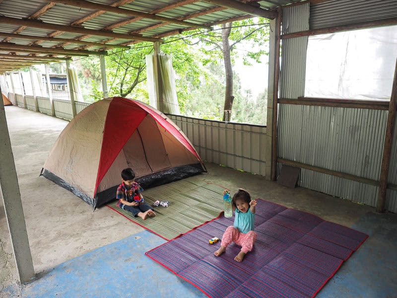 Two young kids sitting on beach mats outside a tent, with canopy above