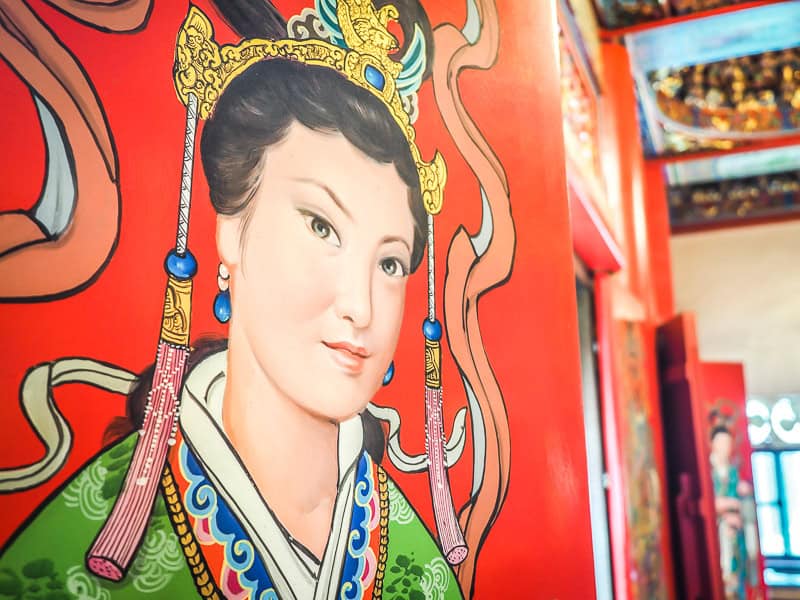 Close up of a painting of a Chinese woman on the inside of a red door in a temple