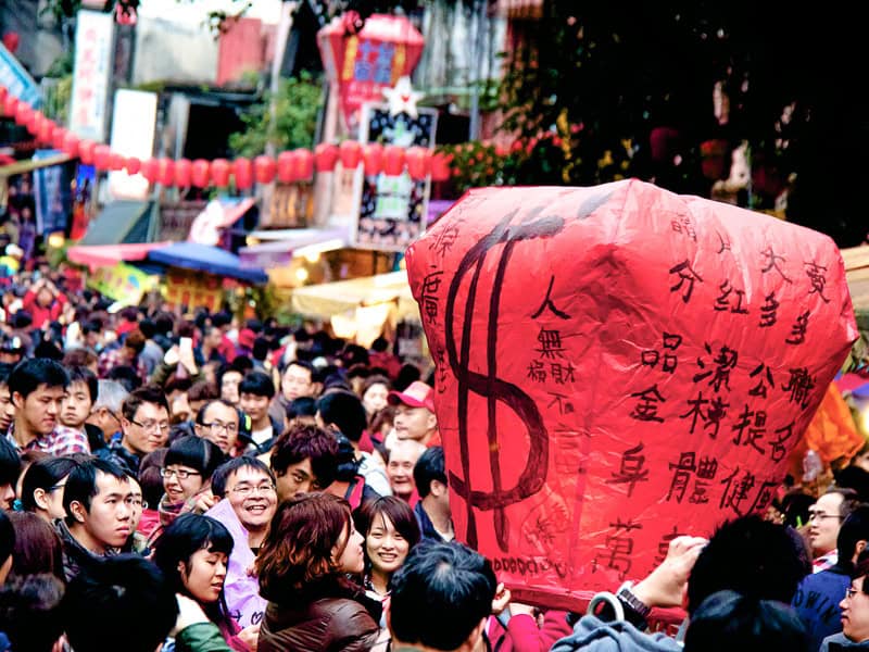 A crowd of people with a large red lantern with a dollar sign painted on it